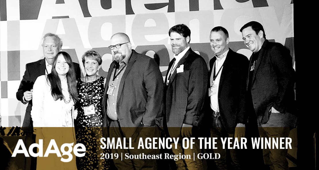 A group of seven people stands on stage at the AdAge Small Agency of the Year awards, Southeast Region, Gold Winner in 2019. They are smiling and posing together in front of a backdrop with the AdAge logo.